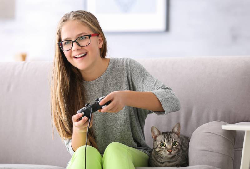 young girl playing video games with her cat beside her