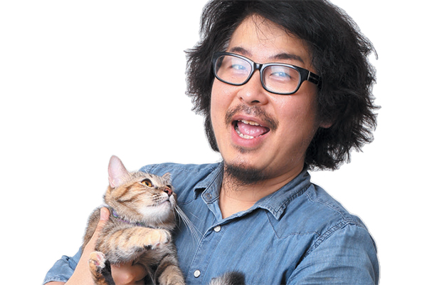 A man with glasses holding a cat that's looking up.
